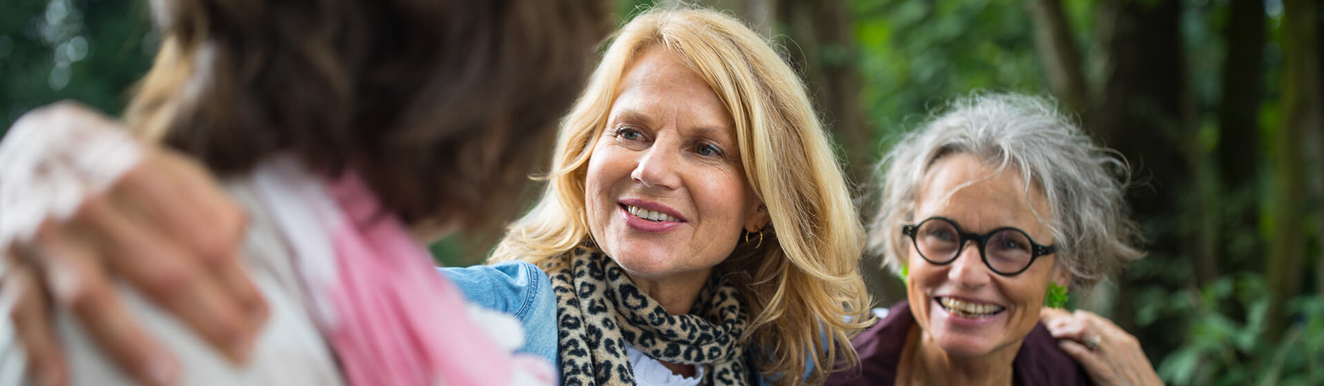 Three mature women friends walking through woods with arms around each other